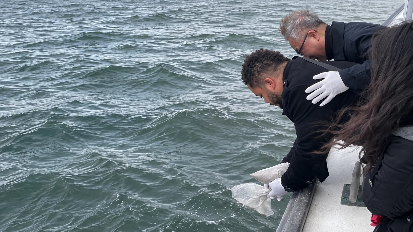 Family members committing cremated remains to the ocean from the side of a vessel